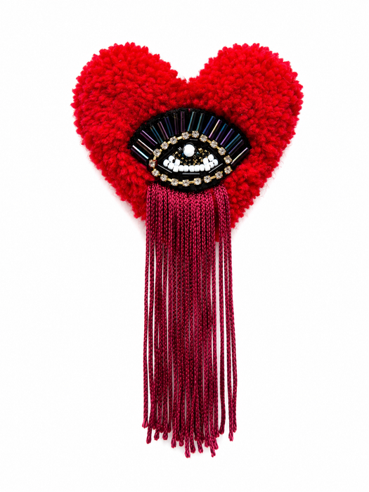 Handmade tufted brooch in vivid red with black evil eye embellishment featuring iridescent bugle bead lashes and deep magenta fringe