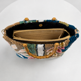A top-down view of a decorative handbag with a multicolored beaded exterior, gold-toned bamboo-style handles, and a black interior lining with a beige pouch, set against a white background.